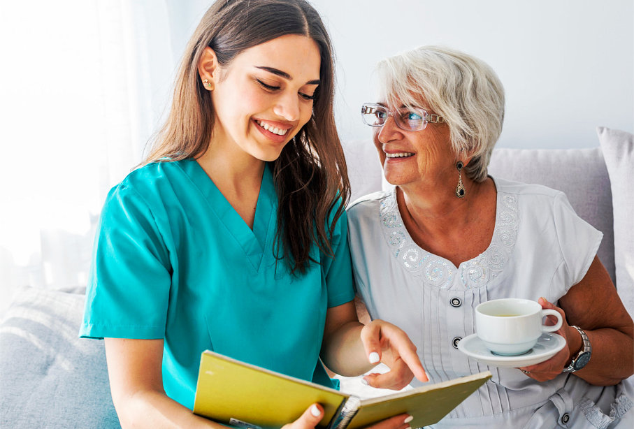 caregiver reading for senior woman who's holding a cup of tea