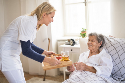 caregiver serving elder woman meal in bed